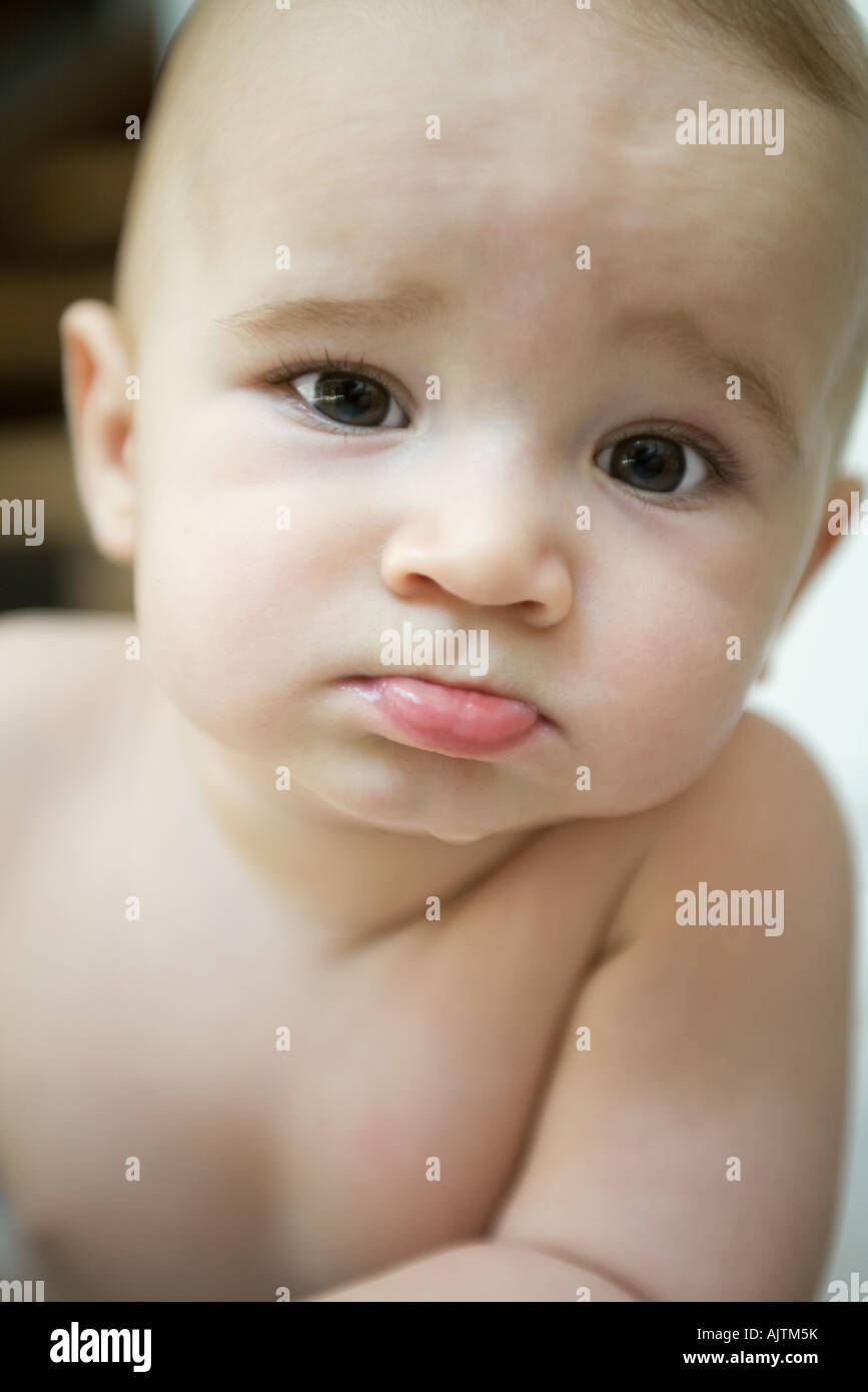 Baby sticking out lower lip and furrowing brow, looking at camera, close-up Stock Photo