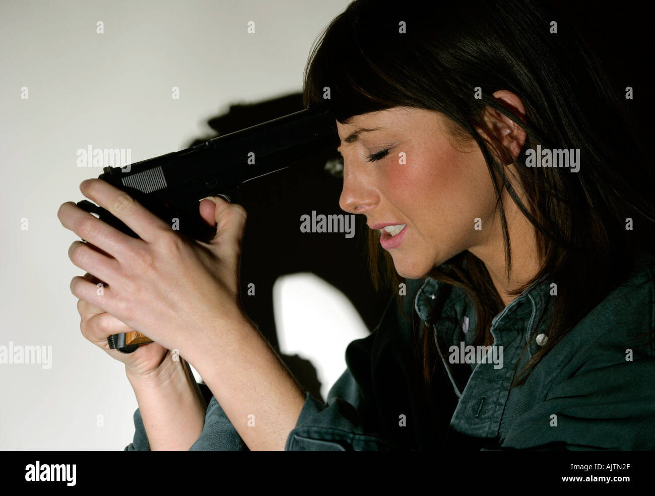 young woman with brown hair holding a handgun to her head Stock Photo