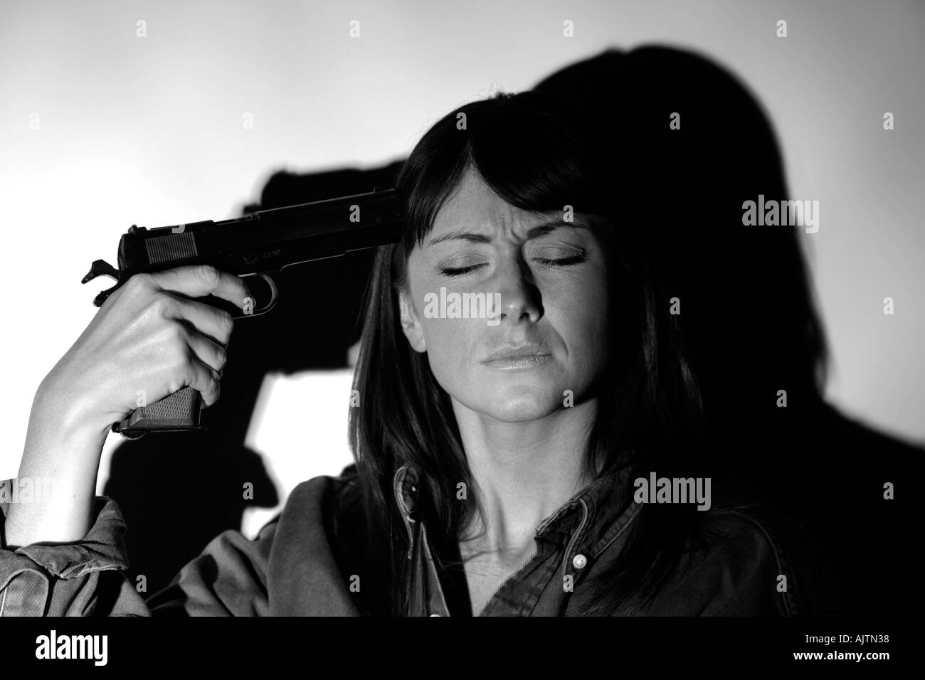 young woman with brown hair holding a handgun to her head Stock Photo