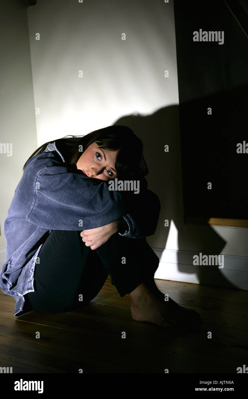 young woman sitting in a pool of light in a corner looking depressed Stock Photo