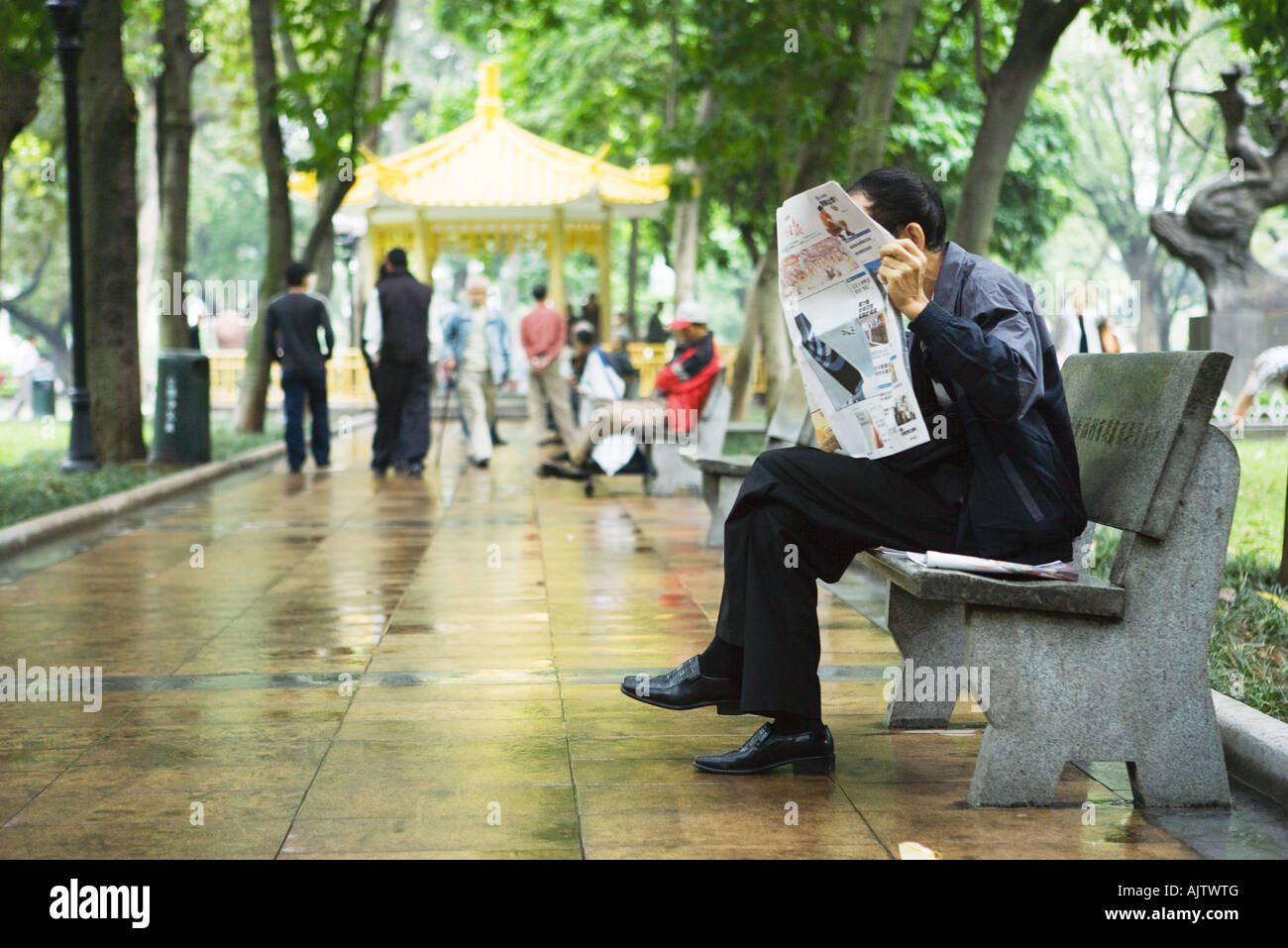 China, Guangdong Province, Guangzhou, man reading newspaper on bench Stock Photo