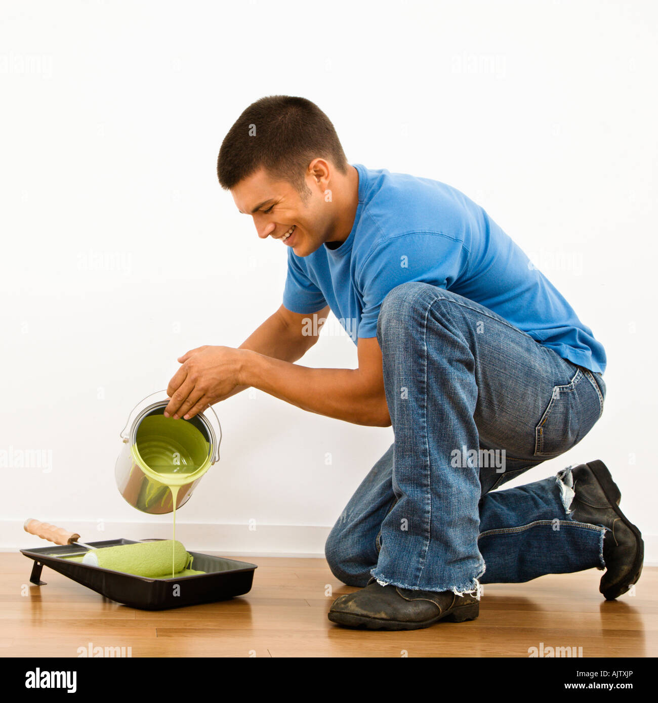 Attractive man smiling and pouring paint into roller pan in home Stock
