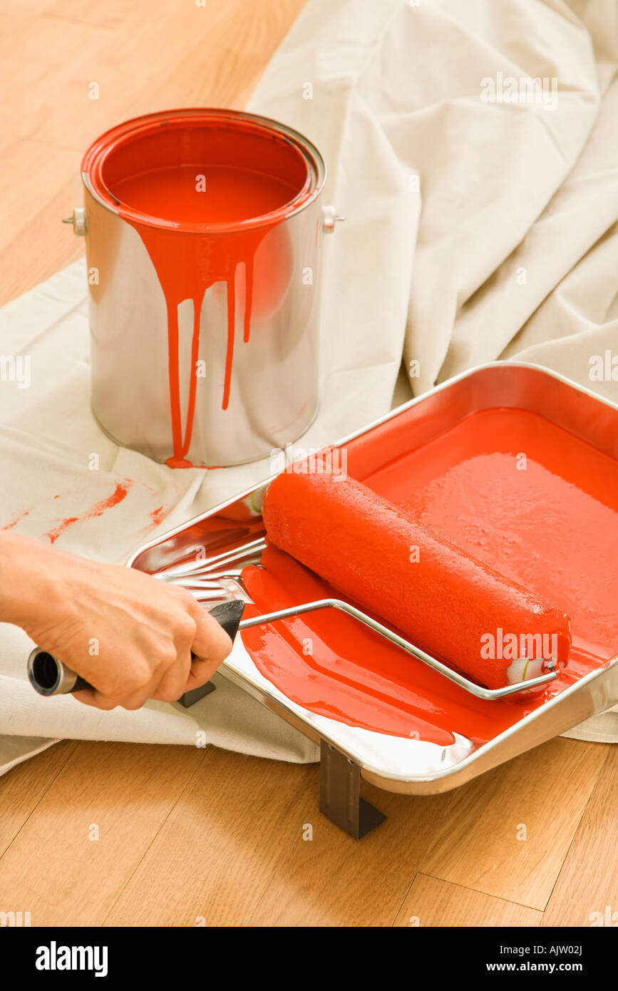Hand holding paint roller in tray with painting supplies on drop cloth Stock Photo
