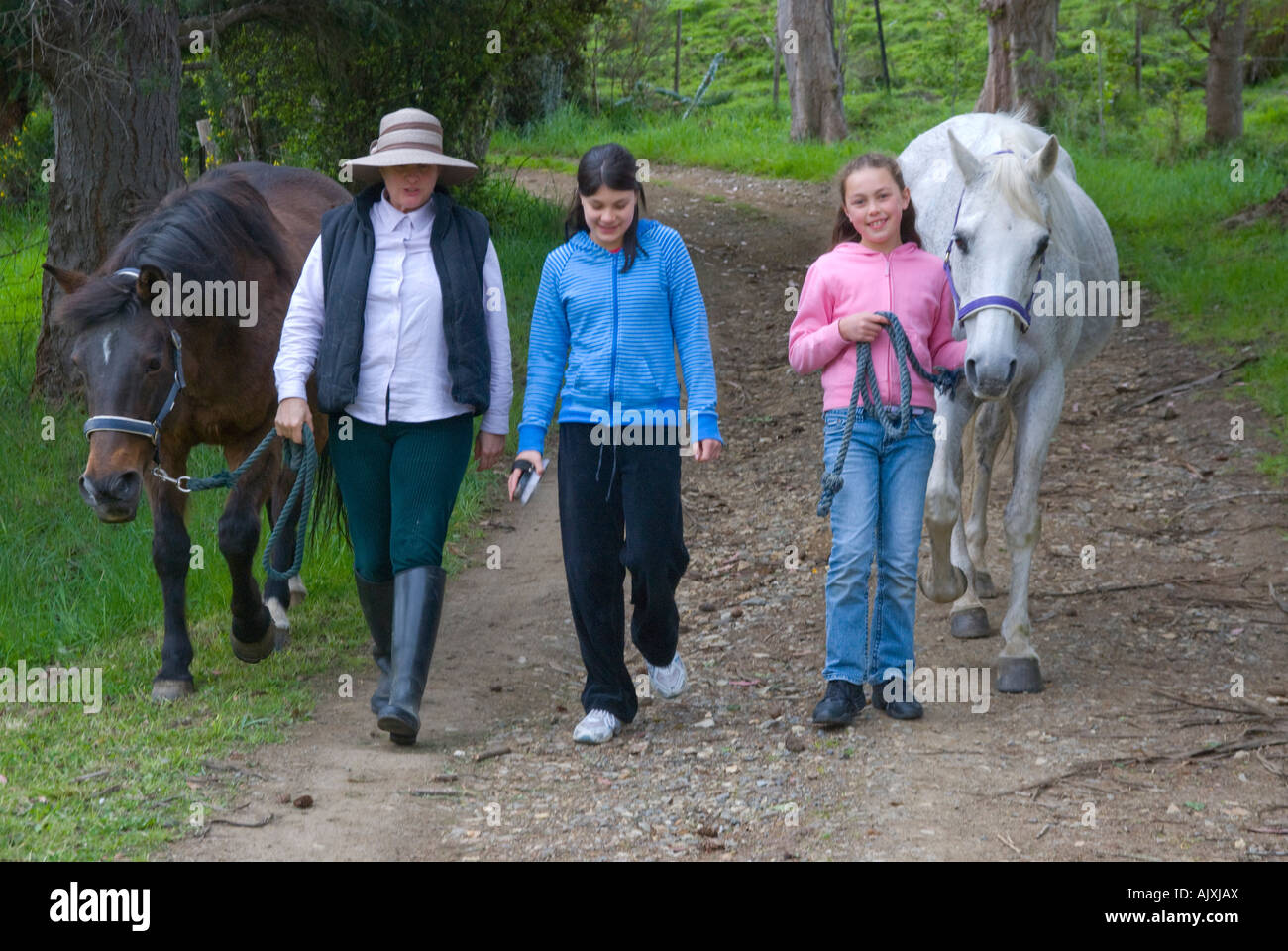 Two young girls and woman leading two horses on a country lane Stock Photo Alamy