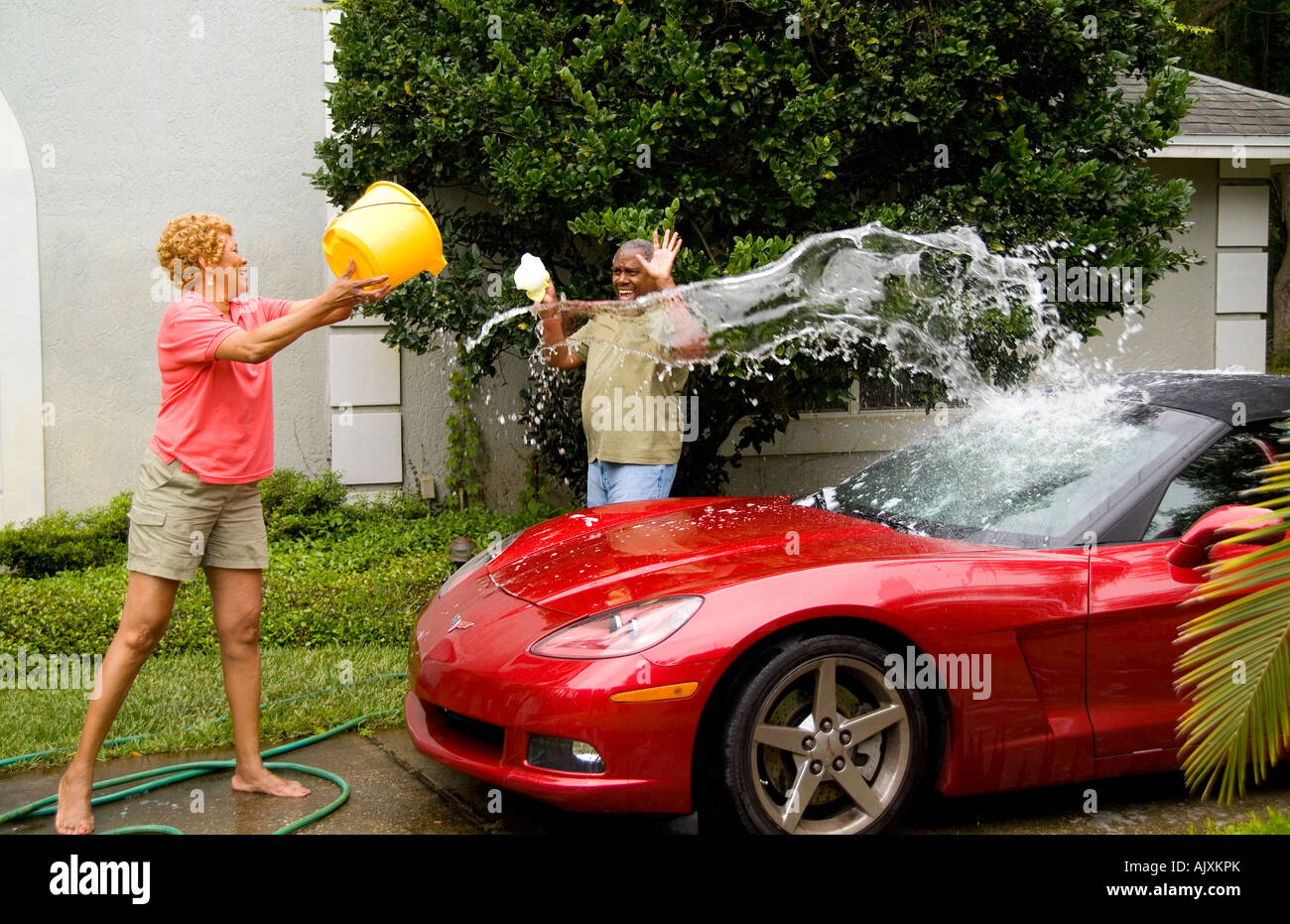 Retired black african american couple having fun nwashing car and splashing water outdoors at home with their Corvette sportscar Stock Photo