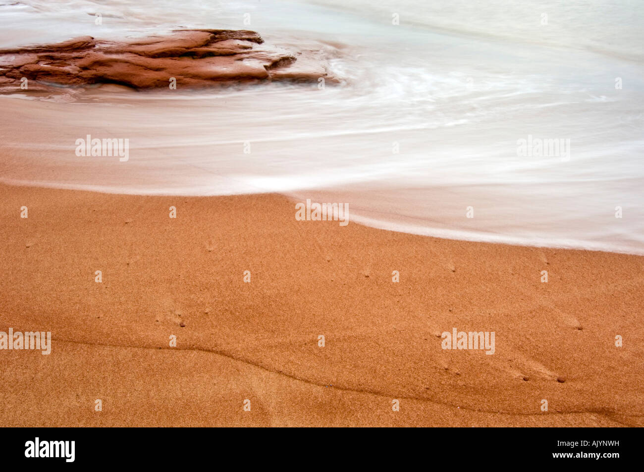 Beach sand and red rocks with  light surf and runoff patterns, Campbell's Cove, PE/PEI Prince Edward Island, Canada Stock Photo