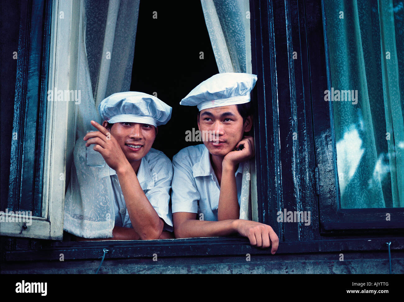 China. Shanghai. Two male chefs looking out from a window. Stock Photo