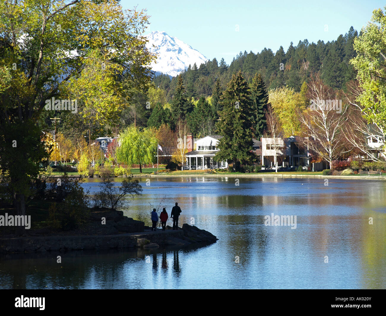 A family walks along Mirror Pond in Drake Park in downtown Bend during the autumn North Sisters Peak is in the background Stock Photo