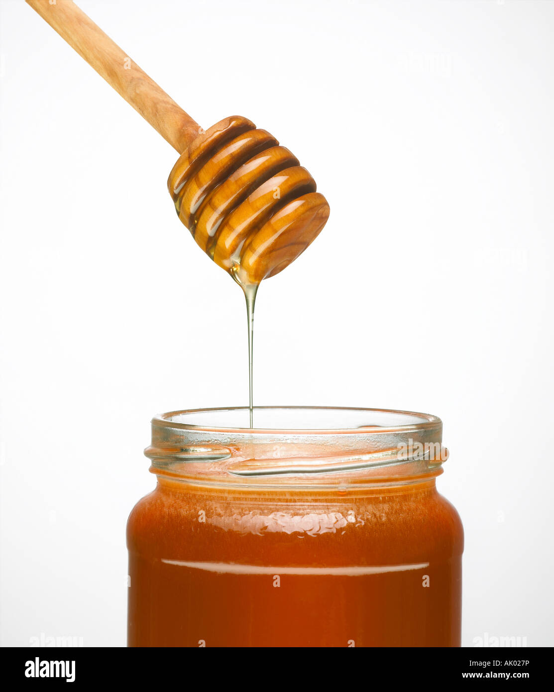 HONEY DRIPPING FROM WOODEN HONEY DRIPPER INTO GLASS JAR OF HONEY Stock Photo