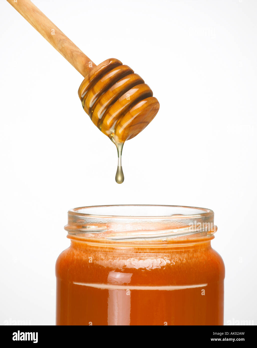 HONEY DRIPPING FROM WOODEN HONEY DRIPPER INTO GLASS JAR OF HONEY Stock Photo