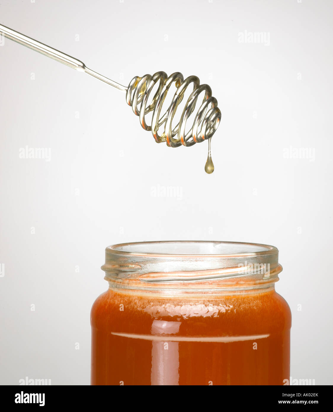 HONEY DRIPPING FROM STEEL HONEY DRIPPER INTO GLASS JAR OF HONEY Stock