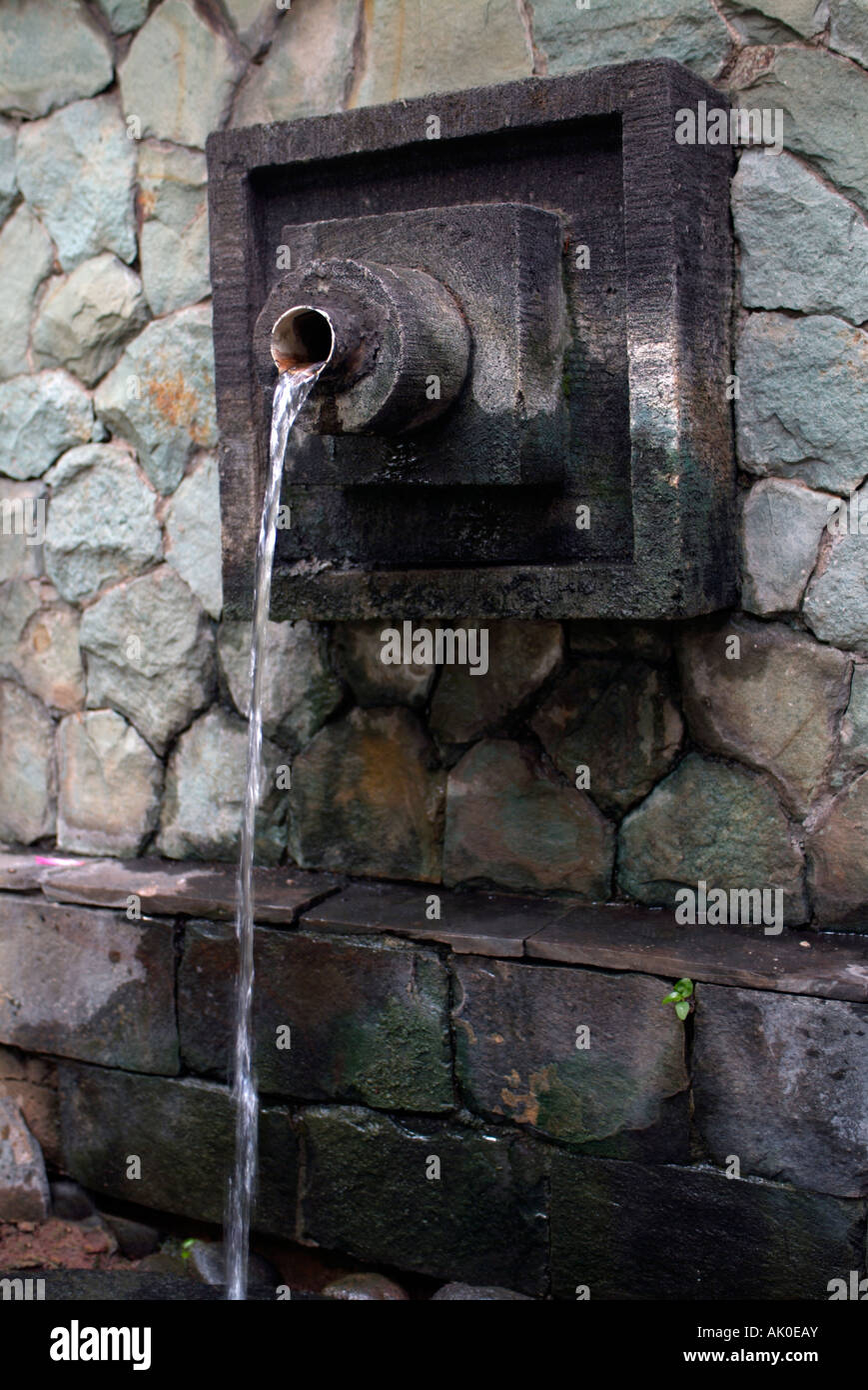 modern looking stone water feature consisting of a round spout set into a square inlayed support Stock Photo