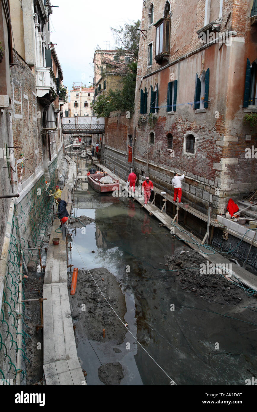 Workers repairing buildings along a drained canal in