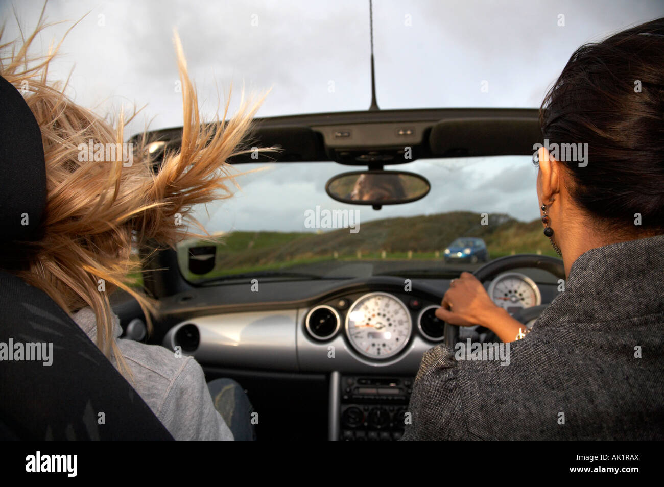 young asian woman driving a mini convertible along the seafront in the evening at speed with blonde haired irish girl Stock Photo