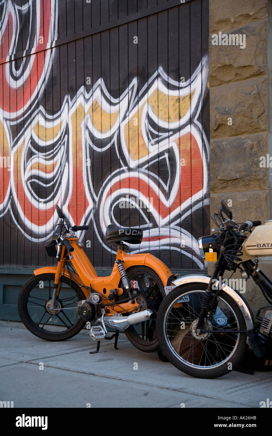 Two mopeds in front of wall with graffiti tagging Stock Photo