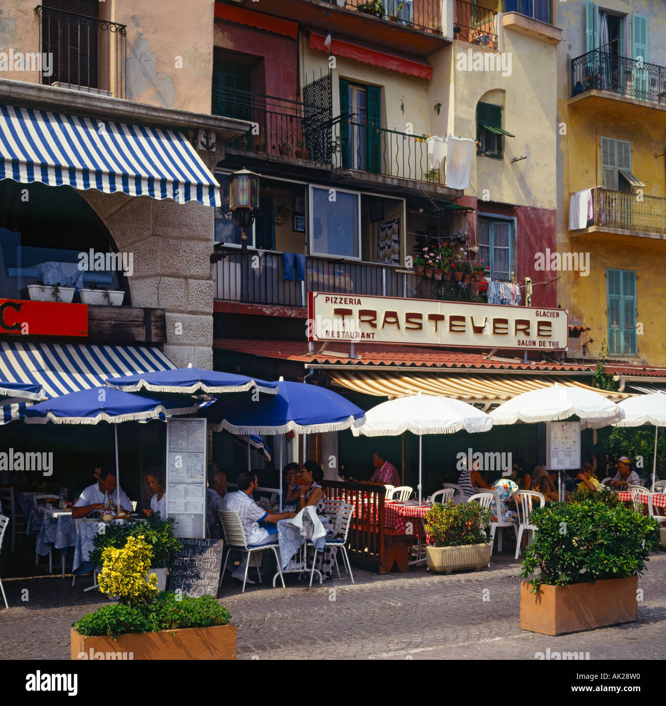 Attractive cafes and restaurants and people dining under fringed sun umbrellas on the waterfront in Villefranche South of France Stock Photo