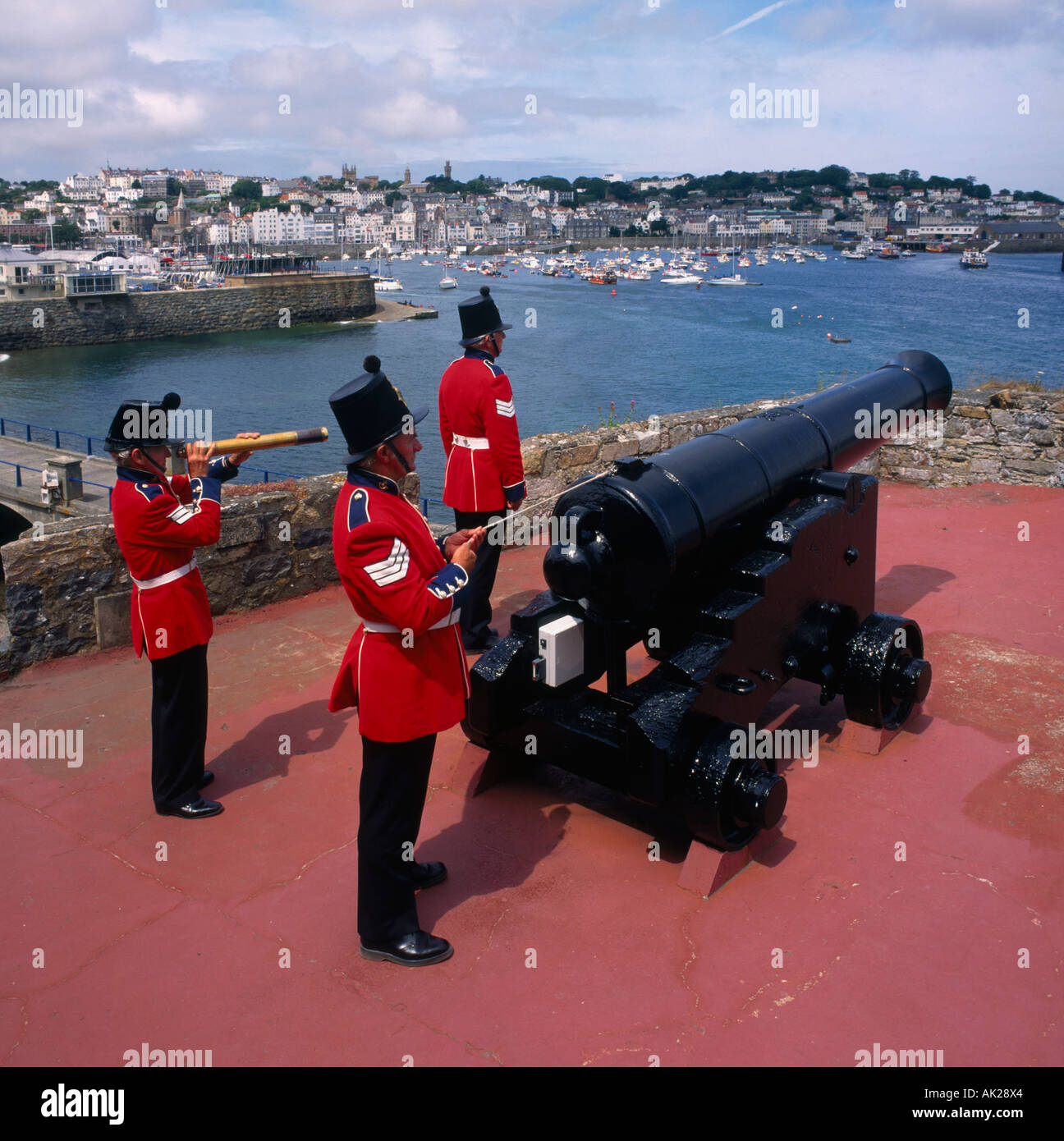 Three soldiers in red military uniform fire The Noon Day Gun artillery salute at Castel Cornet St Peter Port Guernsey Stock Photo