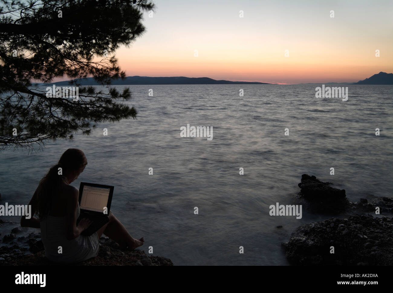 Woman Using a Laptop Computer on the Seashore at Dusk Stock Photo