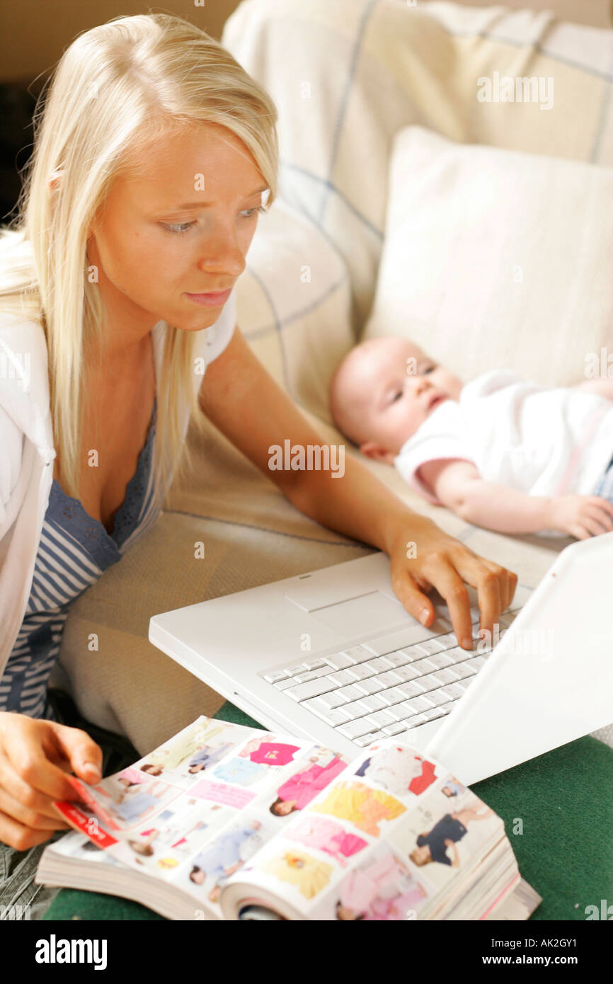 teenage mum ordering from catalogue with baby in background Stock Photo
