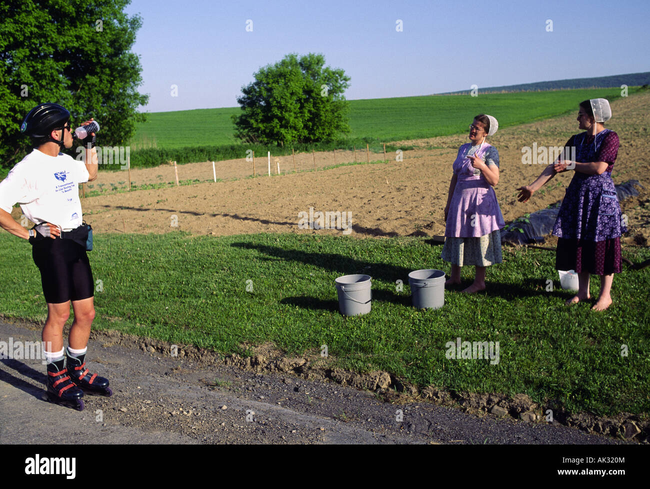 An inline skater stops to talk to two tradionally dressed mennonite women working in a field in Pennsylvania Stock Photo