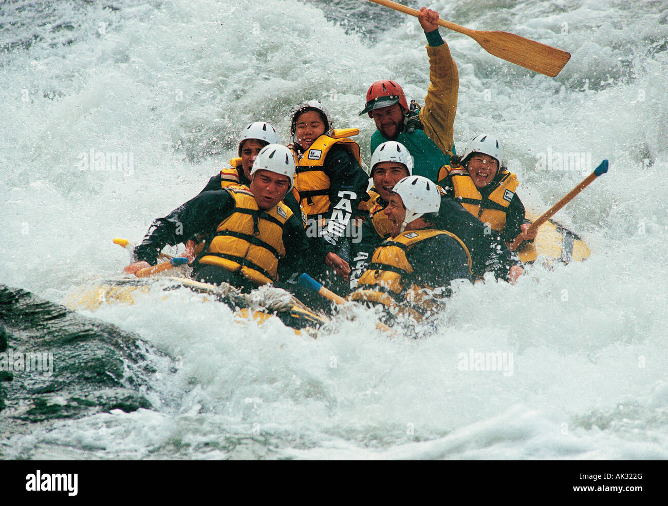 Group of people descending white water river rapids in rubber raft. Stock Photo