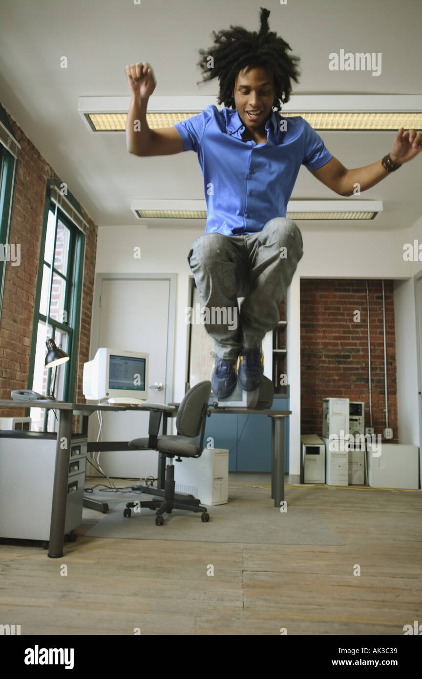 A young man leaping high in the air in a loft style office Stock Photo
