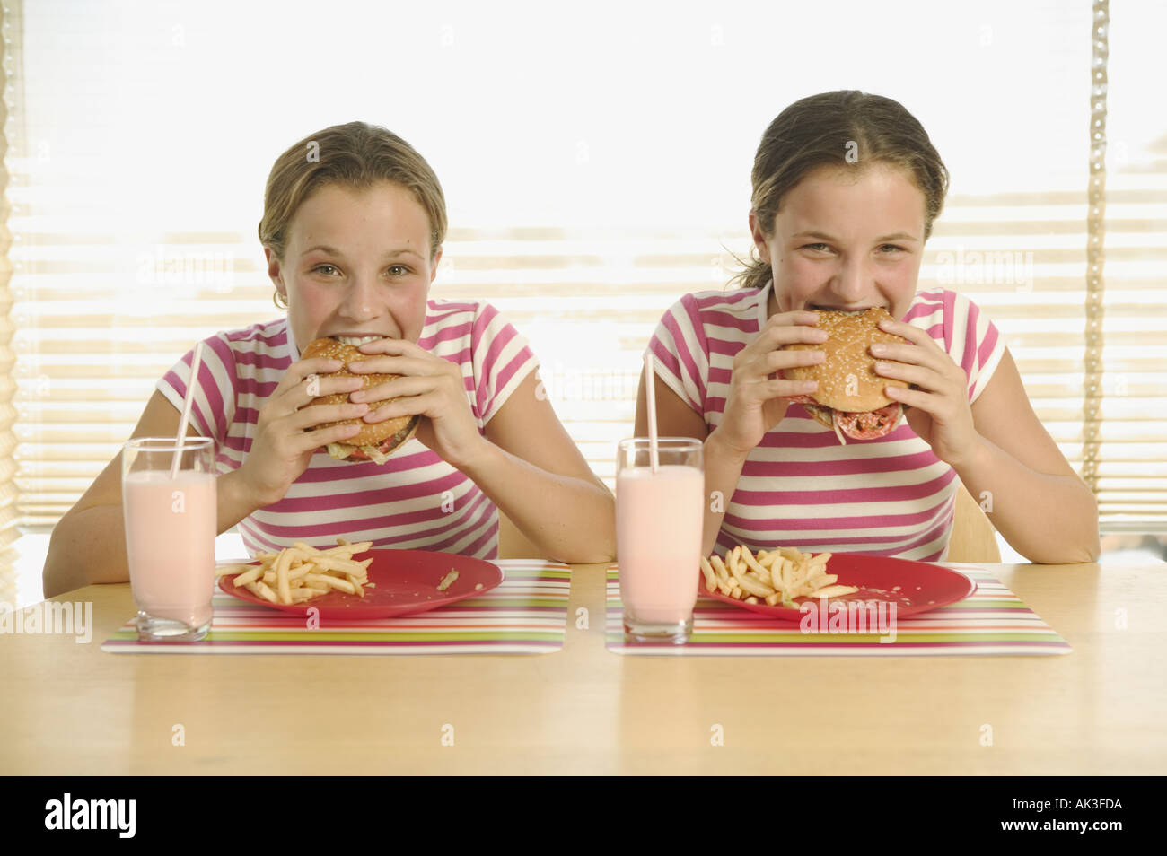 Twin teenage girls eating hamburgers Stock Photo Alamy