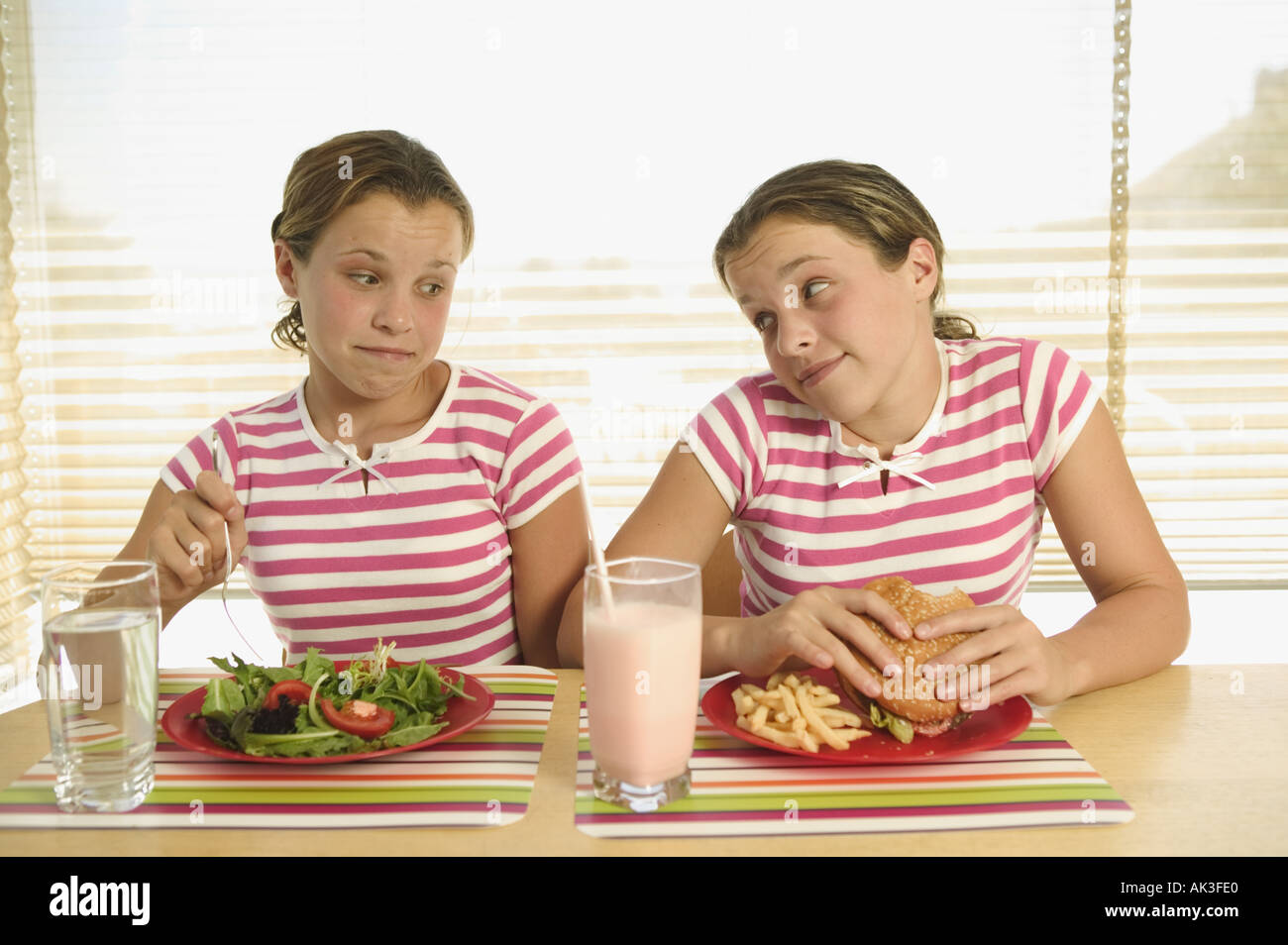 Twin teenagers eating different lunches Stock Photo