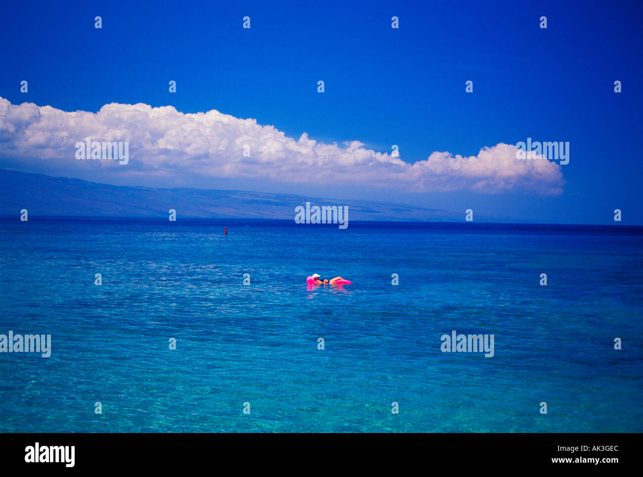 A woman floats aimlessly on an air mattress off the beach in Maui Hawaii Stock Photo