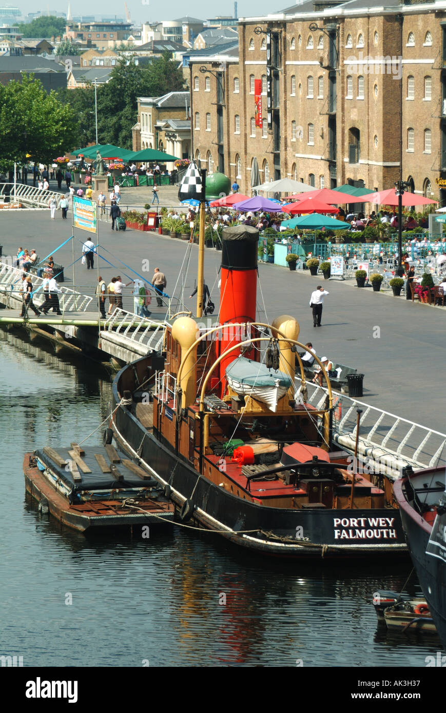 Canary Wharf area of Docklands preserved tug boat with dockside pavement bars and restaurants West India Quay Tower Hamlets East London England UK Stock Photo