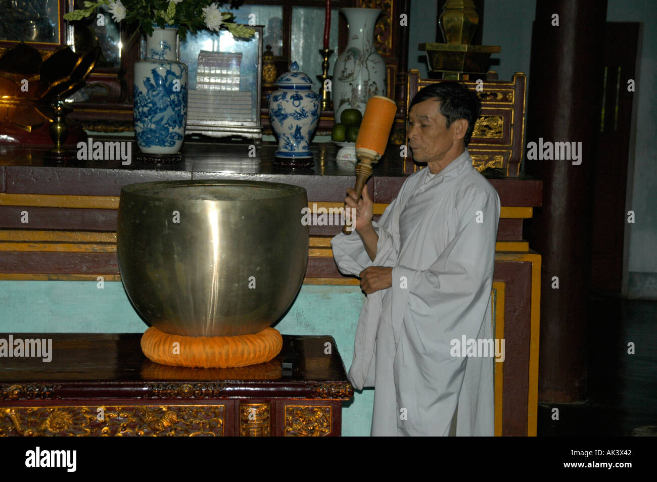 Monk is banging on a big singing bowl in the Temple of the Laughing Buddha Thien Mu Pagoda Hue Vietnam Stock Photo