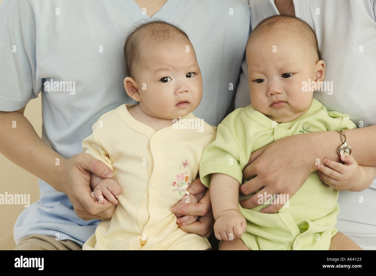 Twins sitting side by side on their parents laps Stock Photo