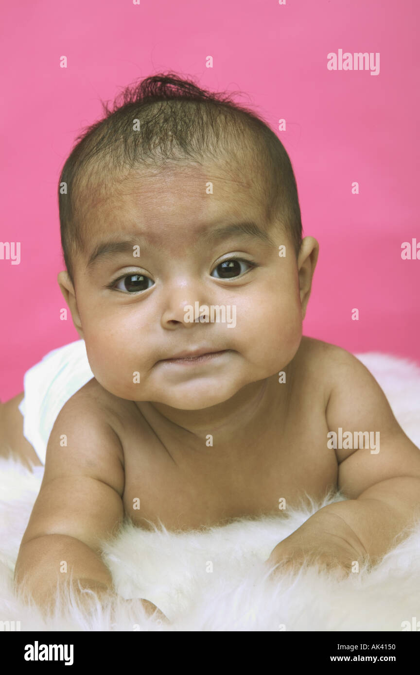 A baby girl lounging on a white rug Stock Photo