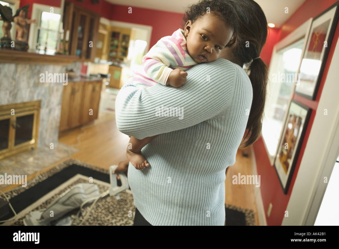 Woman holds baby while vacuuming Stock Photo