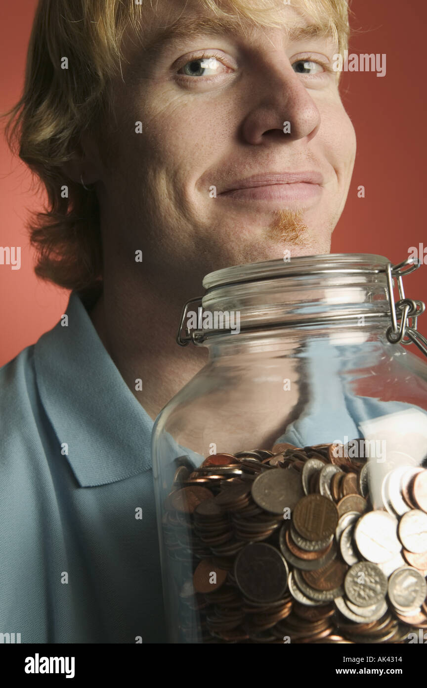 Young man holding a large glass coin jar Stock Photo