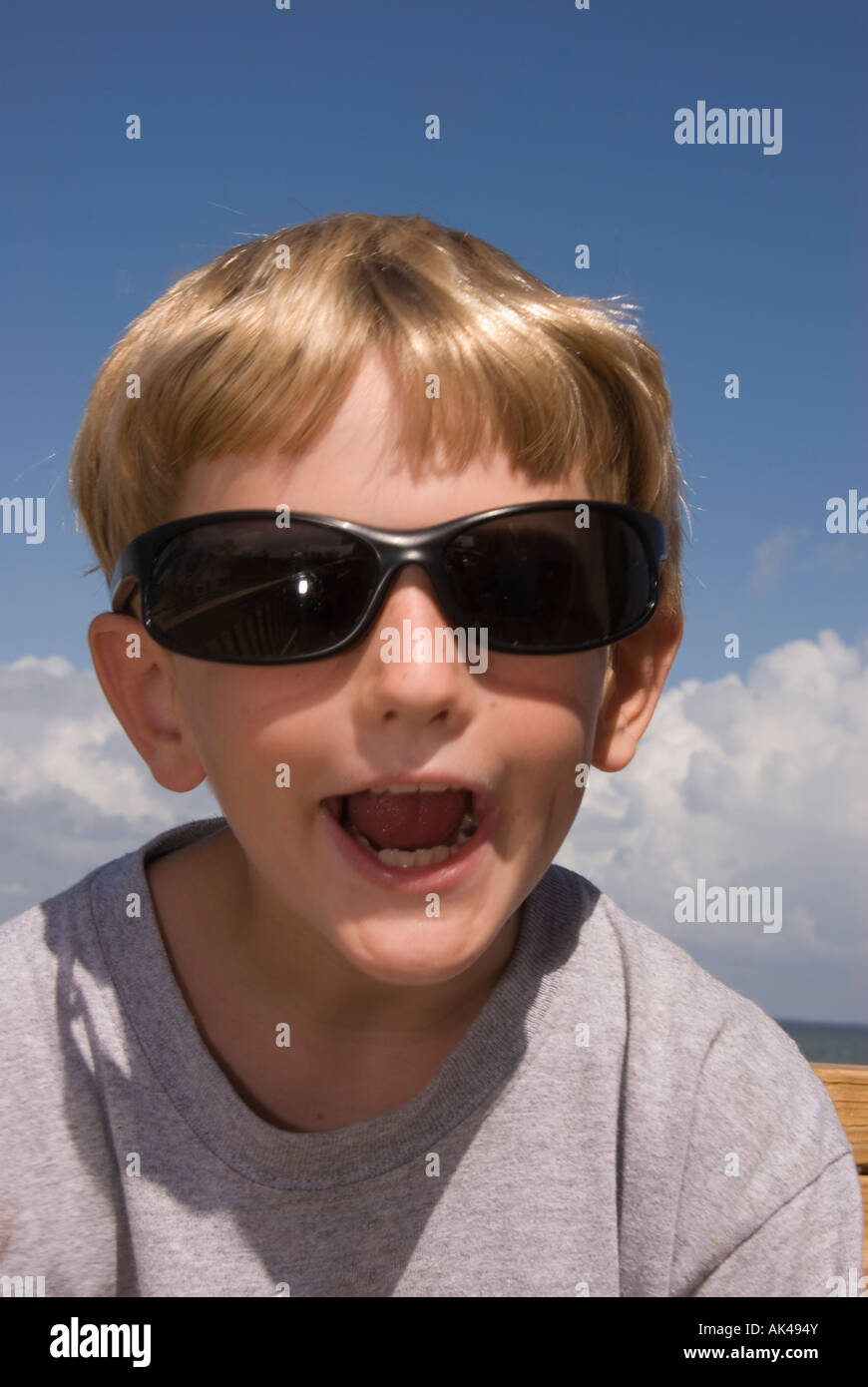 Young boy age 8 summer family vacations dark sunglasses huge smile blond hair open mouth distorted face humor funny Stock Photo