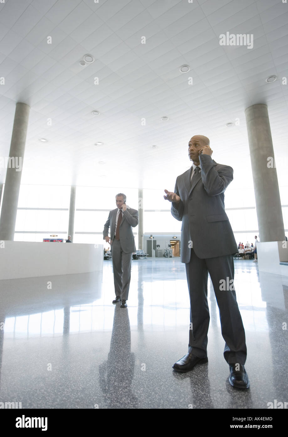 Businessmen using cell phones in airport concourse Stock Photo