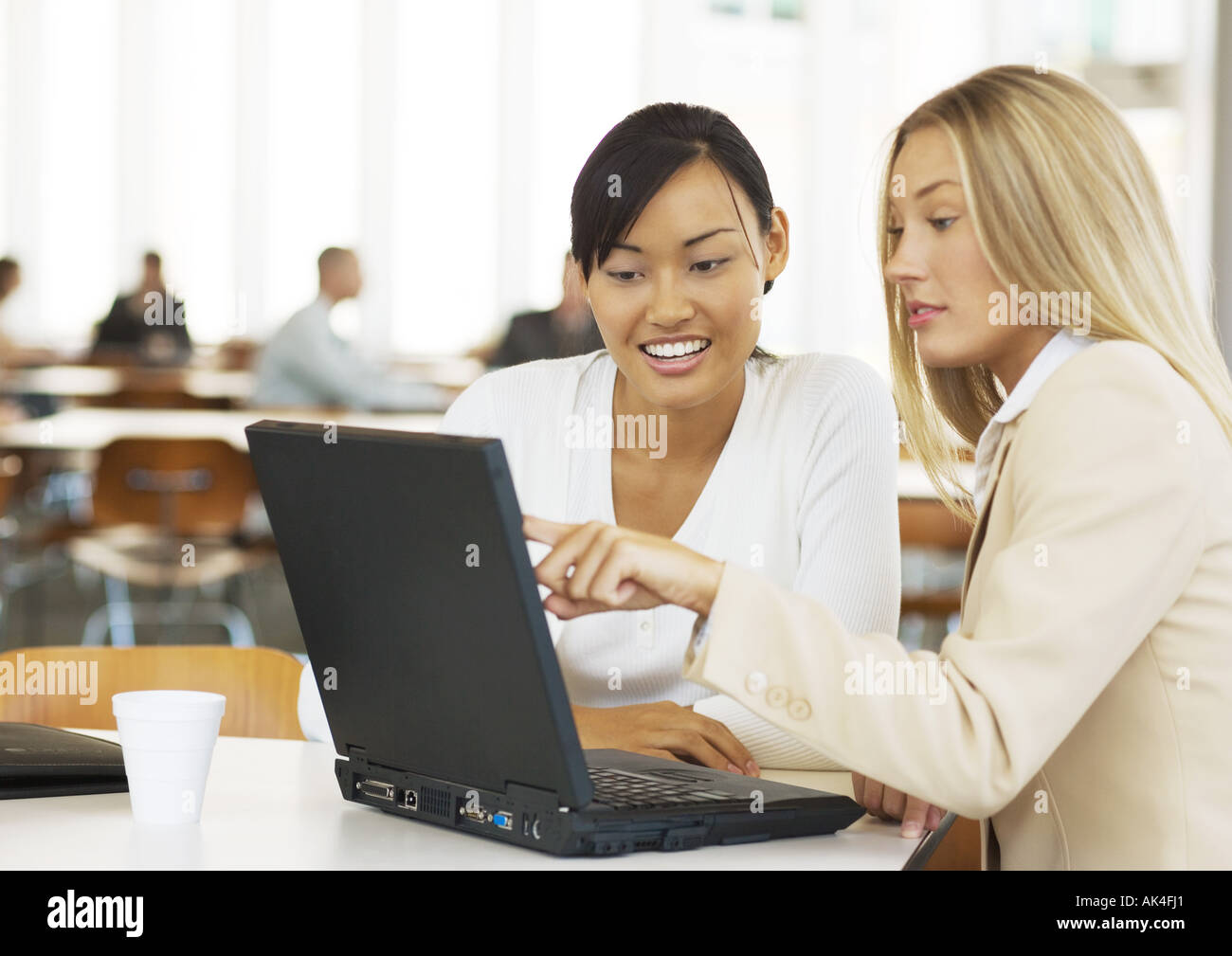 Two young business women using laptop together, smiling Stock Photo - Alamy