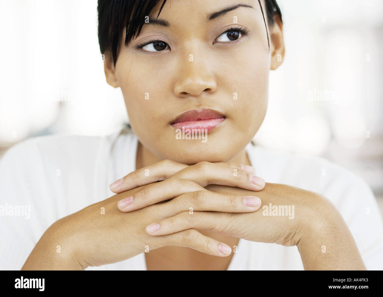 Young woman with hands clasped under chin, looking away Stock Photo Alamy