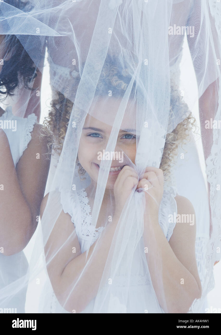 Little girl standing underneath bride's veil Stock Photo