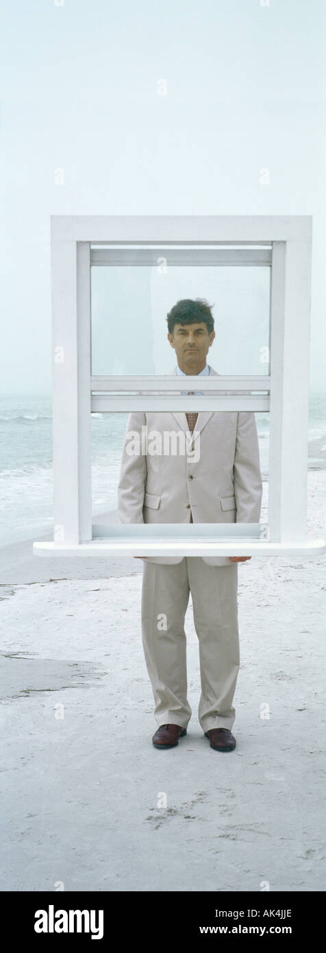 Businessman standing behind window frame on beach Stock Photo