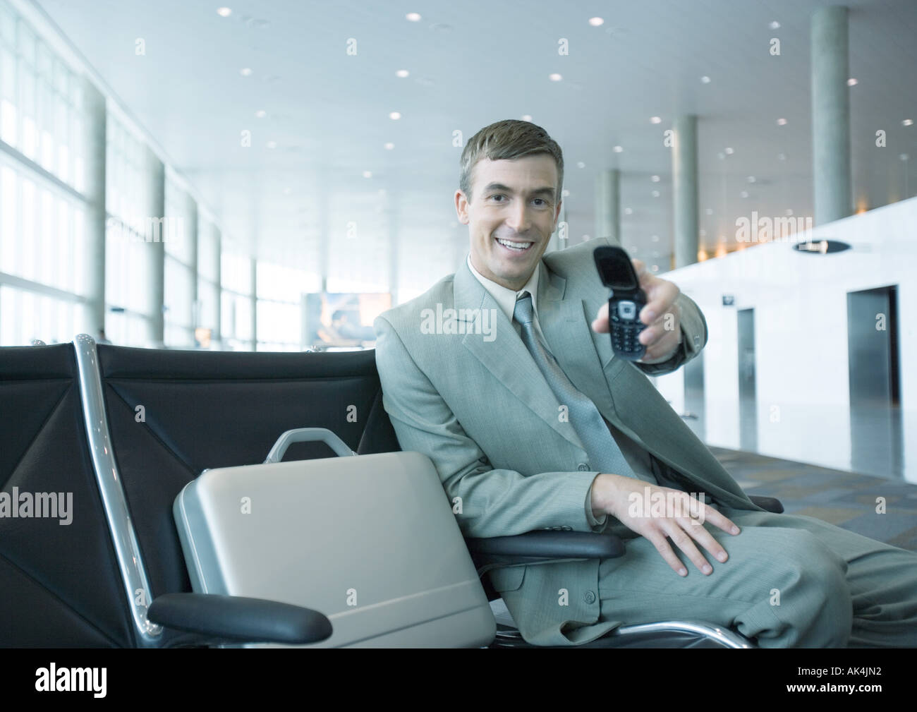 Businessman holding out cell phone in airport lounge Stock Photo