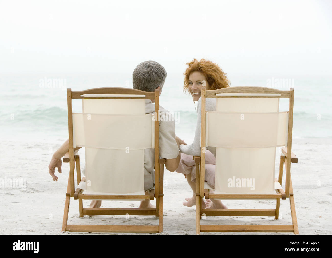 Couple sitting in beach chairs, woman turning around, looking at camera Stock Photo