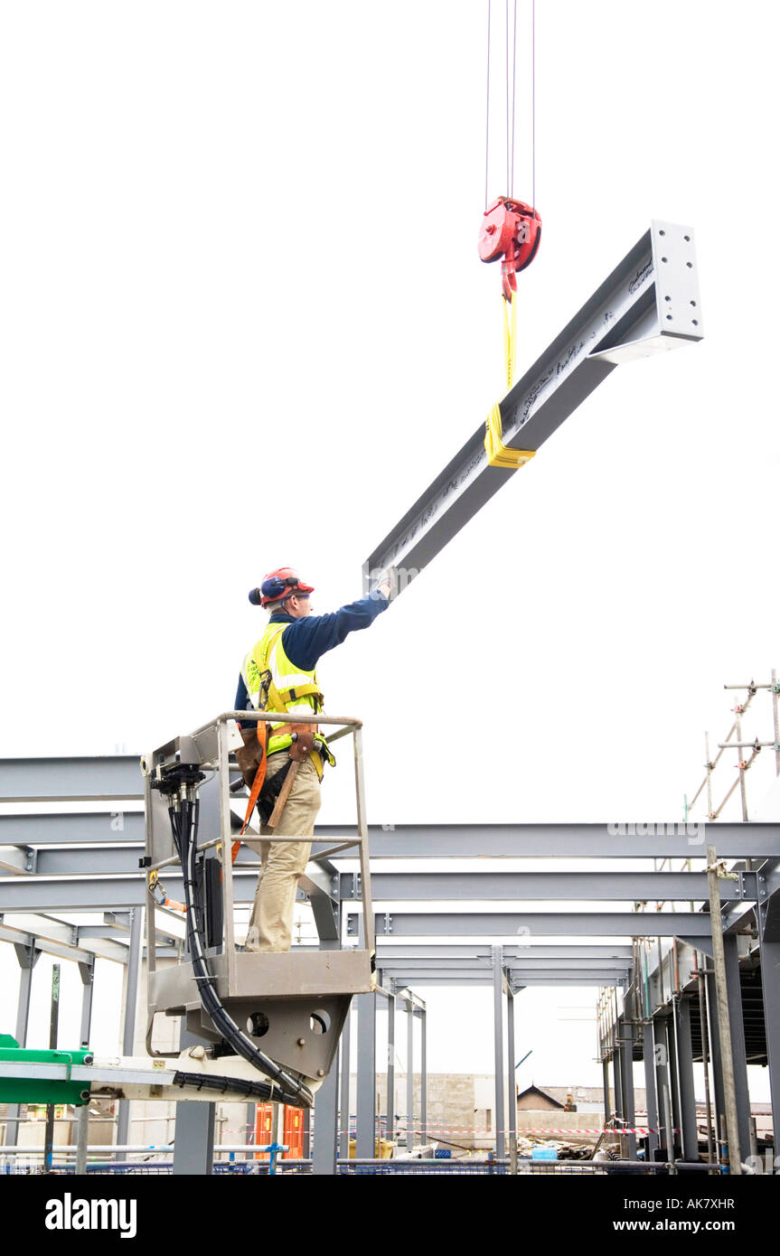 Man on hydraulic platform positioning steel girder being lowered down by crane on a construction site Stock Photo
