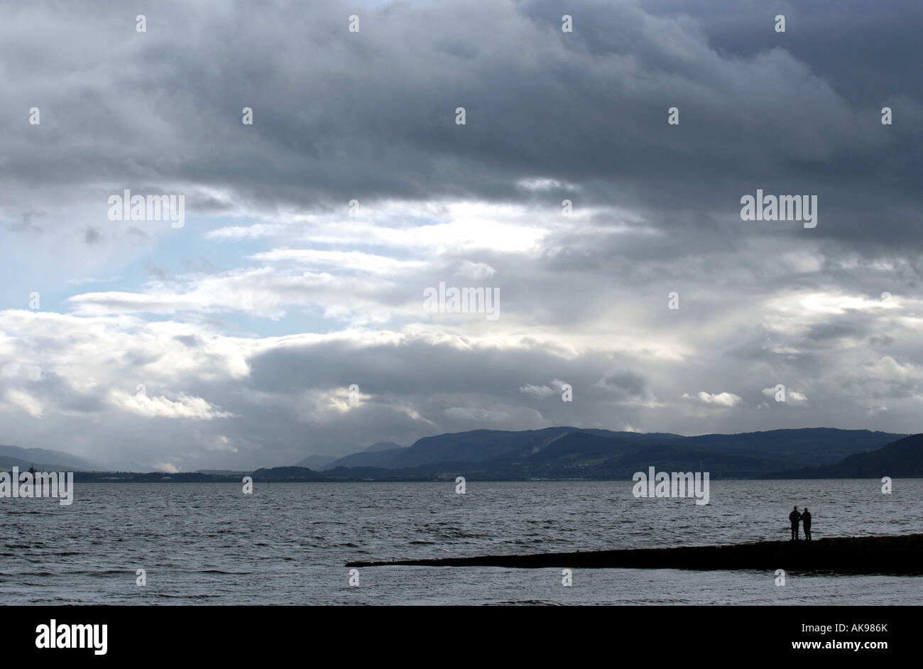 A COUPLE LOOK OUT TOWARDS CLOUDY SKIES OVER INVERNESS FROM THE JETTY AT CHANONRY POINT IN THE MORAY FIRTH,NORTH EAST SCOTLAND,UK Stock Photo