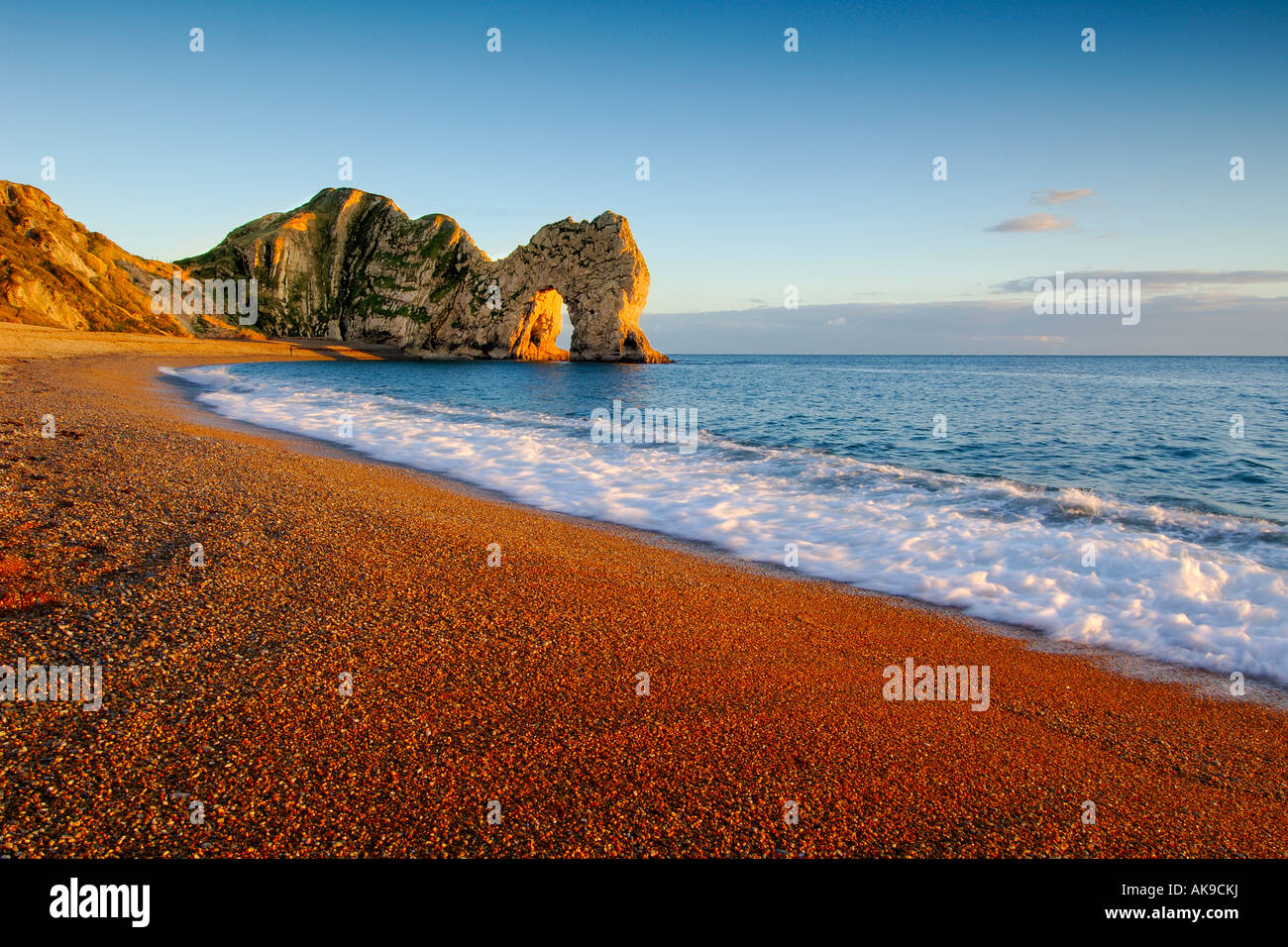 Warm light at sunset on the Dorset coast looking East towards Durdle Door with a clear blue sky Stock Photo