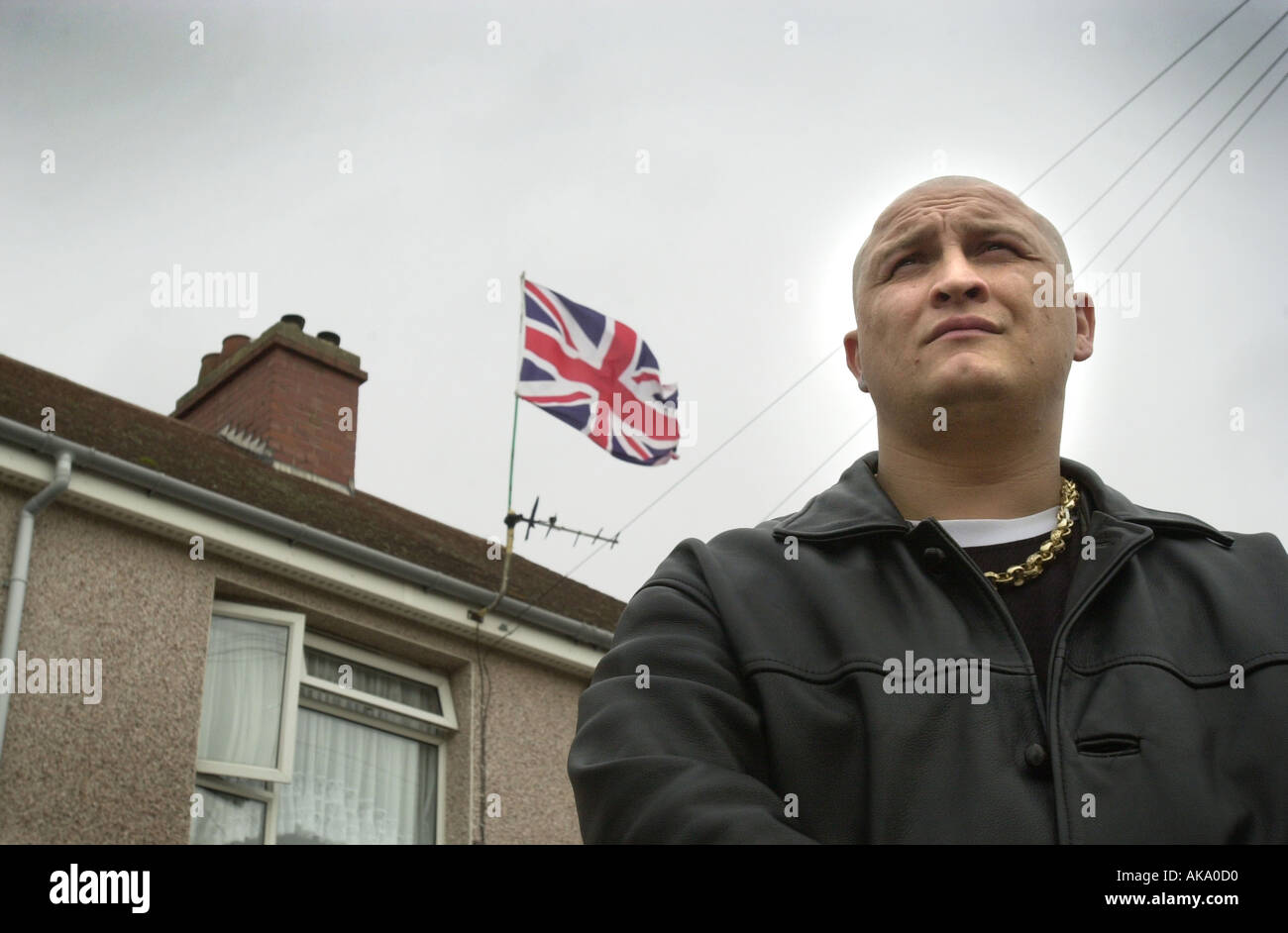 A skinhead stands outside a house that is flying the Union flag UK Stock Photo