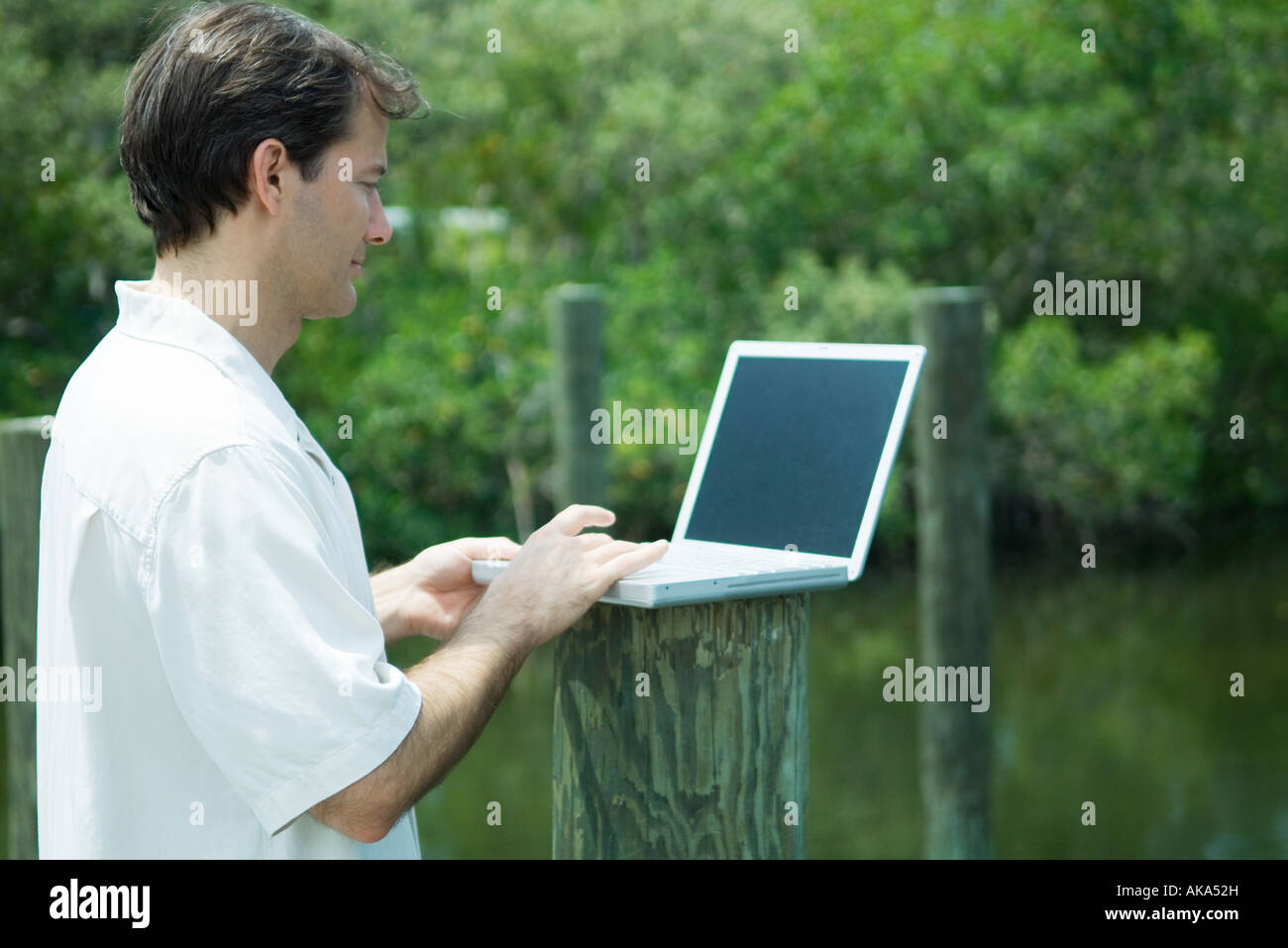 Man using laptop computer outdoors, next to lake Stock Photo - Alamy