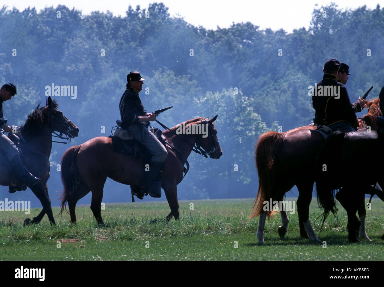 Magnificent horses silhouetted against a blue smoky forest as cavalry soldiers cross the open green fields of the battlefield Stock Photo