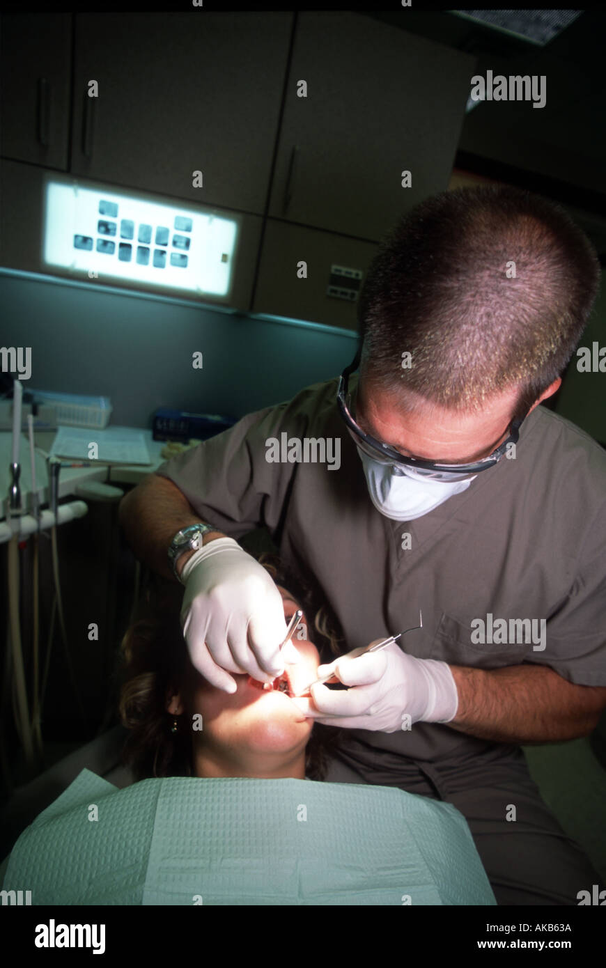 With tooth x rays in the background watching closely and wearing tight latex gloves a professional dentist performs an oral exam Stock Photo